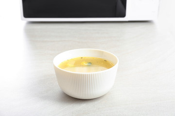 Bowl with soup near microwave on table
