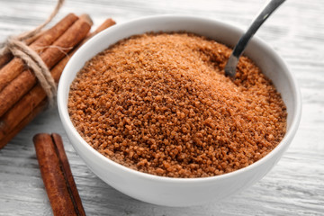 White bowl with cinnamon sugar and sticks on wooden background