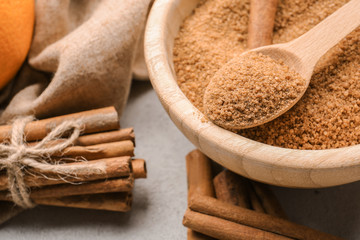 Cinnamon sticks and sugar in wooden bowl with spoon on grey background, closeup