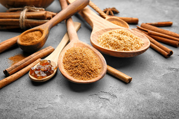 Composition with cinnamon sticks, sugar and powder in wooden spoons on grey background