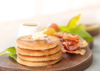 Pancakes with butter and bacon on wooden board