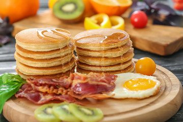 Tasty breakfast with pancakes, fried egg and bacon on wooden board