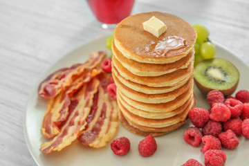 Tasty breakfast with pancakes, bacon and fruits on table