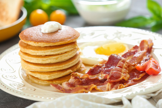 Tasty breakfast with pancakes, fried egg and bacon on table