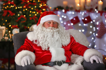 Authentic Santa Claus sitting in armchair at room decorated for Christmas