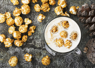 A glass of mouth-watering sweet milk coffee with a creamy foam topped with caramel crispy popcorn on a gray stone background. Selective focus.