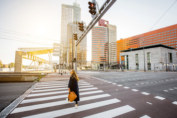 Stylish businesswoman crossing the street at the modern district during the morning in Rotterdam city - obrazy, fototapety, plakaty
