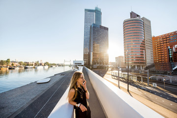 Lifestyle portrait of a stylish woman standing with phone on the modern bridge with skyscrapers on...