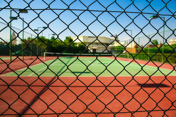 Beautiful tennis court at sunny day, view through mesh fence