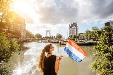 Poster Jonge vrouwelijke toerist die achteruit staat met Nederlandse vlag in de oude haven in de stad Rotterdam © rh2010