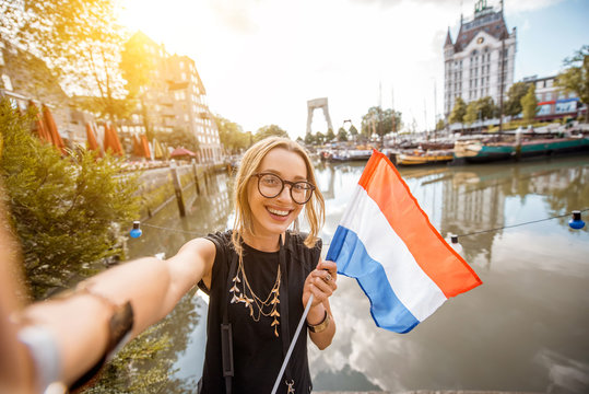 Young woman tourist making selfie photo with dutch flag standing at the old harbor in Rotterdam city