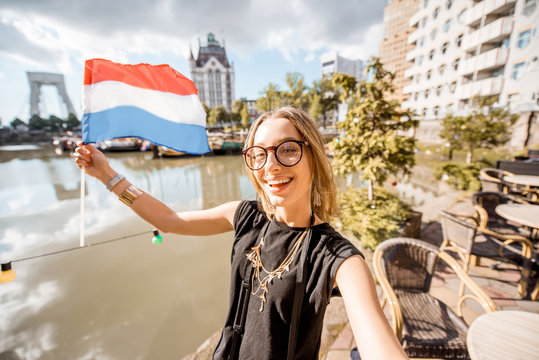 Young woman tourist making selfie photo with dutch flag standing at the old harbor in Rotterdam city