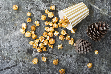 Appetizing golden caramel popcorn in paper striped cups in the New Year's interior with fir cones,...