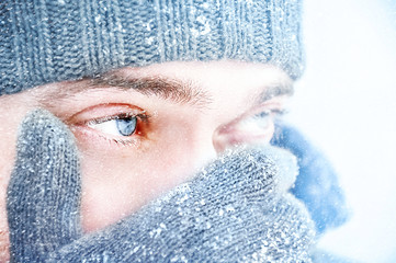 Portrait of a man with blue eyes against a background of falling snow. Beautiful snowy weather. Snowing. Selective focus.