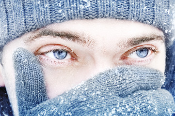 Portrait of a guy with blue eyes against a background of falling snow. Beautiful snowy weather....