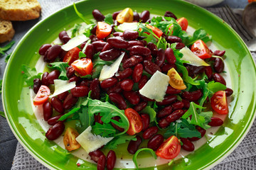 Red beans and wild rocket healthy salad with cherry tomatoes, sea salt flakes and parmesan shavings drizzled with olive oil
