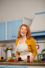 Happy mid aged housewife cooking in kitchen at home. Woman smiling cooking vegetables.