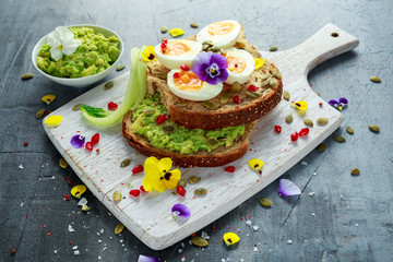 Tasty sandwich with avocado boiled eggs, pumpkin seed and edible viola flowers in a white board. healthy food