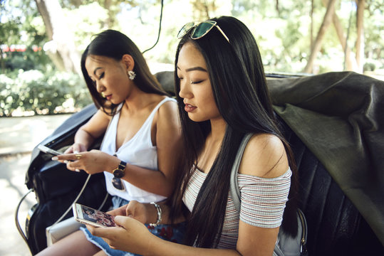 Women sitting in carriage looking at screens.