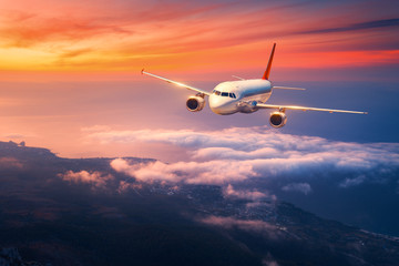 Naklejka premium Passenger airplane. Landscape with big white airplane is flying in the sky over the clouds and sea at colorful sunset. Passenger aircraft is landing at dusk. Business trip. Commercial plane. Travel