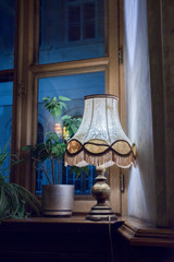  romantic lit lamp with classic lampshade standing in the window at dusk