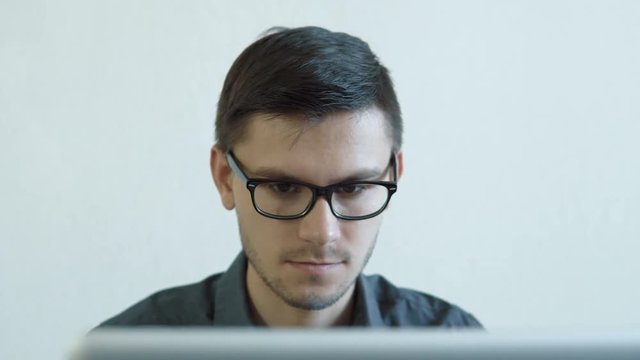 Portrait of a young man wearing glasses sitting in his office in front of a monitor - working on a computer. People stock footage slider shot. 