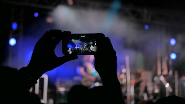 Unrecognizable hands silhouette taking photo or recording video of live music concert with smartphone. Photography, entertainment and technology concept
