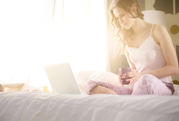 Young beautiful woman sitting in bed with laptop.