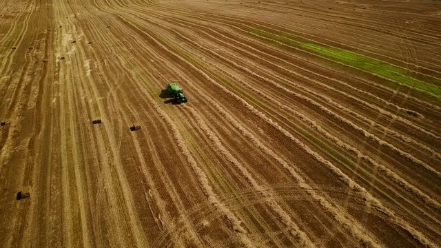 4K. Modern tractor makes haystacks on the field after harvesting. Aerial view.