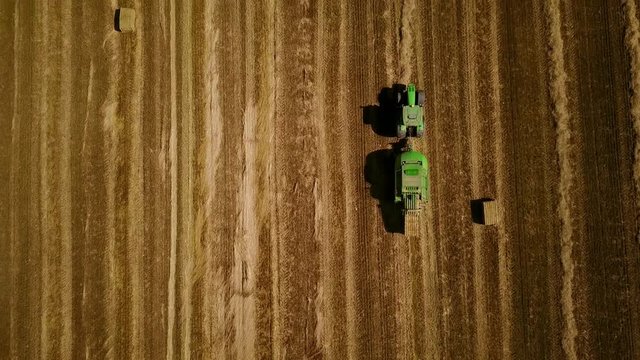 4K. Modern tractor makes haystacks on the field after harvesting. Aerial top view.