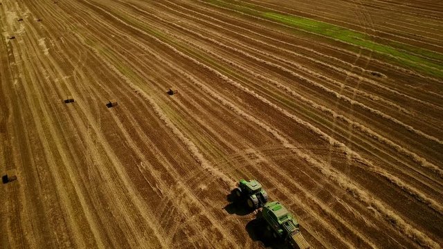 4K. Modern tractor makes haystacks on the field after harvesting. Aerial view.