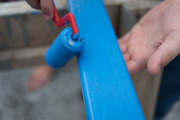 Hand holding board while being painted with blue paint