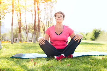 Fototapeta premium Senior woman doing yoga exercise on green grass in the park.