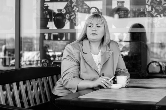 A pretty big European girl with overweight smokes in an outdoor cafe. Problems of smoking among women. The effect of smoking on weight and shape
