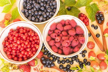 Fresh and colorful berries assortment with green leaves on the light wooden background.