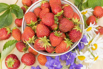 Bowl with beautiful fresh strawberries and colorful flowers on the wooden table.
