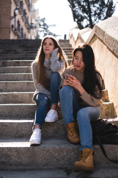 Chinese and european young and pretty women looking at the smartphone in the streets of Madrid, Spain