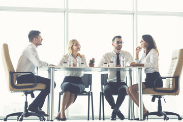 The four business people sit at the office table near the panoramic window