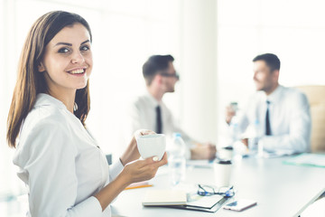 The businesswoman with a cup of coffee sit near colleagues