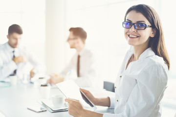 The businesswoman with a tablet sit near colleagues on the sunny background