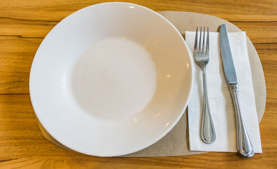 Empty white plate with spoon and knife on wooden background
