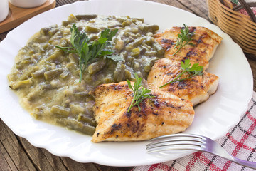 Grilled chicken breasts with cooked green beans in plate on table