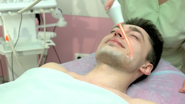 Skin treatment with darsonval device. Young man smiling, beauty clinic. Stimulating collagen production.