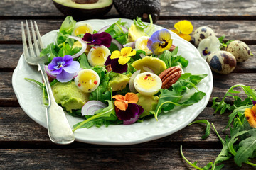 Healthy summer salad with quail eggs, avocado, pecans, wild rocket, red onion and edible viola flowers.