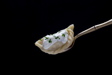 Ukrainian and Russian dishes - vareniki or dumplings with mashed potatoes or cottage cheese and sour cream on a spoon on a black background