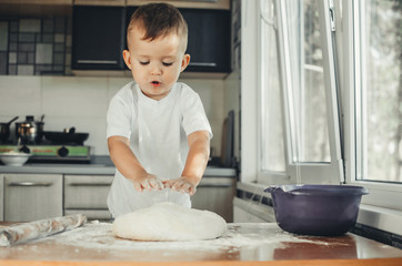 The little Boy in the kitchen hard kneads the dough