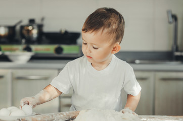 Fototapeta premium The little Boy in the kitchen hard kneads the dough