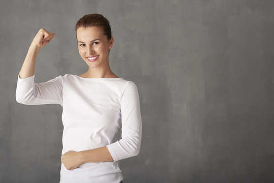 Attractive young woman portrait. Shot of an attractive young woman with her arms raised in celebration while standing at grey wall. 