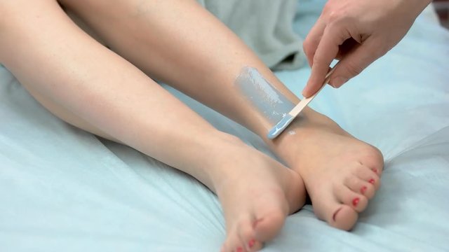 Cosmetician applying hair removal cream. Female legs, epilation.