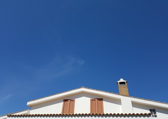 roof of the cute white house with brown windows against blue sky